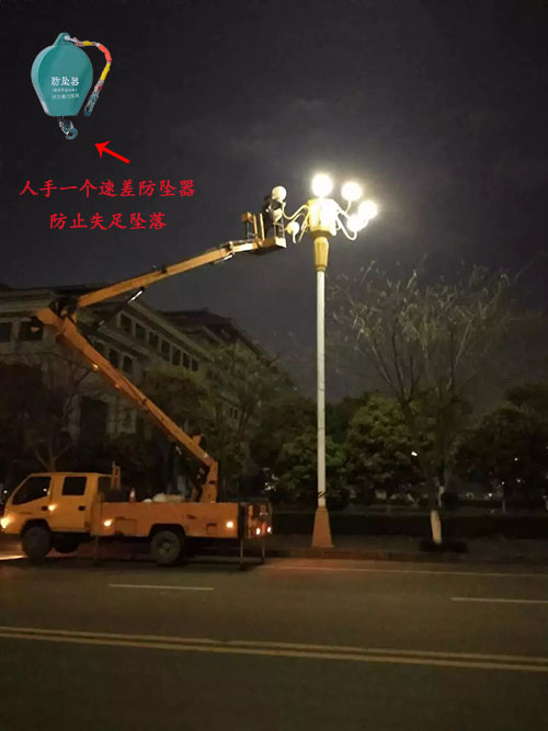 夜晚工人佩戴速差防墜器進行高空維修路燈